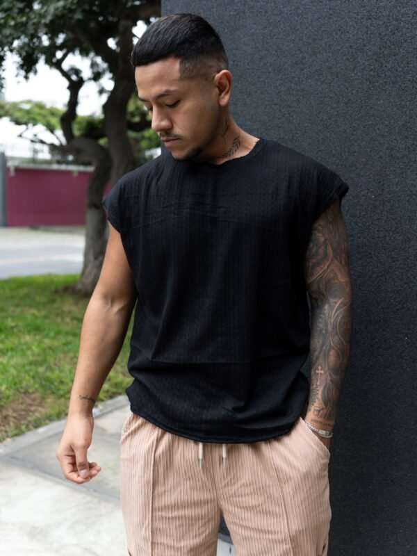 Hombre vistiendo polo negro Manica Zero de Ezzeta, con diseño sin mangas y estilo urbano.